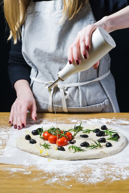 Der Küchenchef gießt Olivenöl auf die rohe Focaccia.