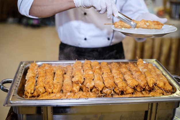 Der Küchenchef legt die heiße Platte mit duftendem Hähnchenfleisch-Schaschlik auf Spieße in Nahaufnahme