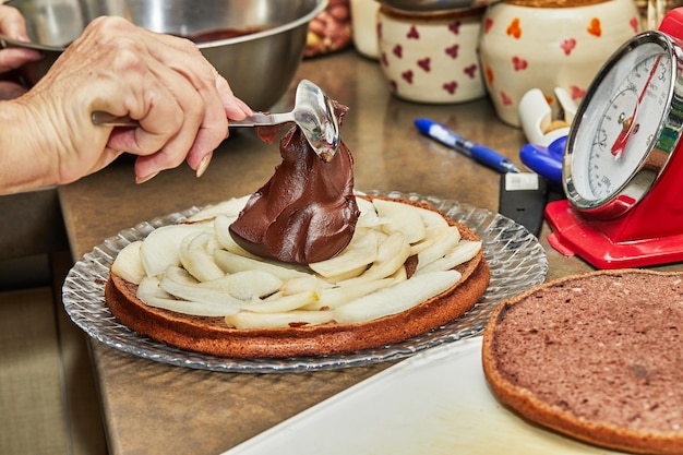 Der Küchenchef legt Schokoladenganache über die Birnen in der Torte, um eine Schokoladentorte mit Birnen und Walnüssen zuzubereiten