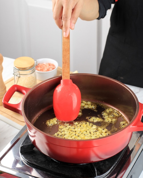 Der Küchenchef rührt weiße gehackte Zwiebeln, die in einem holländischen Ofen aus rotem Gusseisen gebraten werden