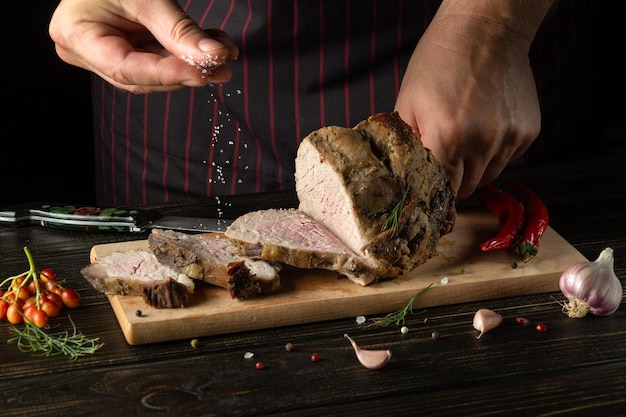 Der Küchenchef salzt das gebackene geschnittene Rindfleisch auf dem Küchenschneidebrett Platz für Hotelfleischrezepte oder Restaurantmenüs auf schwarzem Hintergrund