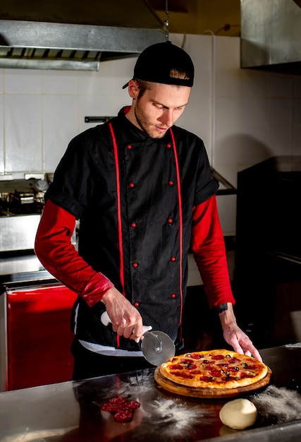 Der Küchenchef schneidet die Pizza zum Servieren mit einem Messer