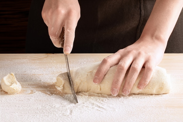 Foto der küchenchef schneidet mit einem messer auf einem mit mehl bestreuten holztisch ein stück teig aus einem ganzen teig