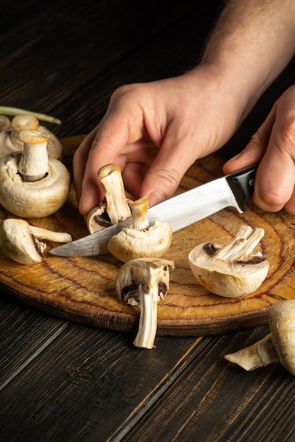 Der Küchenchef schneidet Pilze mit einem Messer auf einem Schneidebrett Vegetarisches Essen oder Menü für das Hotel