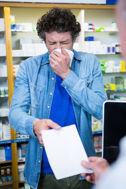 Foto der kunde niest, während er dem apotheker ein rezept gibt
