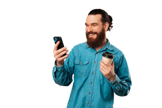 Der lachende bärtige Mann genießt die Kaffeepause, während er auf seinem Telefon surft
