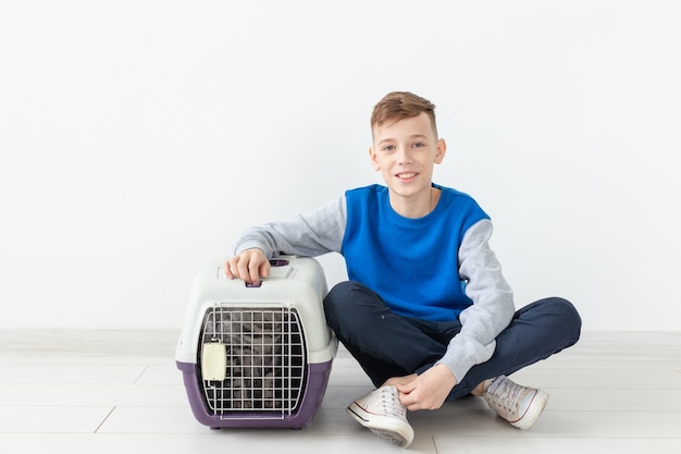Der lachende kleine positive Junge hält einen Käfig mit einer schottischen Katzenfalte neben sich, die auf dem Boden sitzt