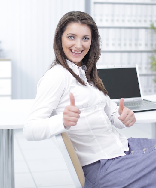 Der lächelnde Angestellte zeigt einen Daumen hoch und sitzt am Schreibtisch im Büro