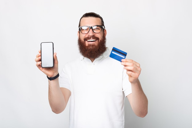 Der lächelnde bärtige Mann mit Brille zeigt der Kamera den Bildschirm des Telefons und der Karte, die er verwendet.