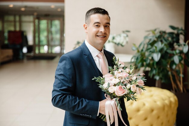 Der lächelnde Bräutigam mit einem Blumenstrauß in den Händen sieht irgendwo hin