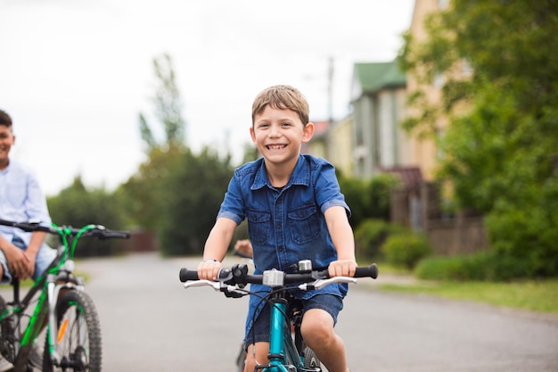Der lächelnde kleine Junge sitzt auf einem Fahrrad Die glücklichen Freunde radeln in der Stadt