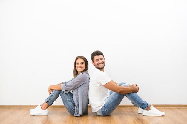 Der lächelnde Mann und die Frau sitzen auf dem Hintergrund der leeren Wand