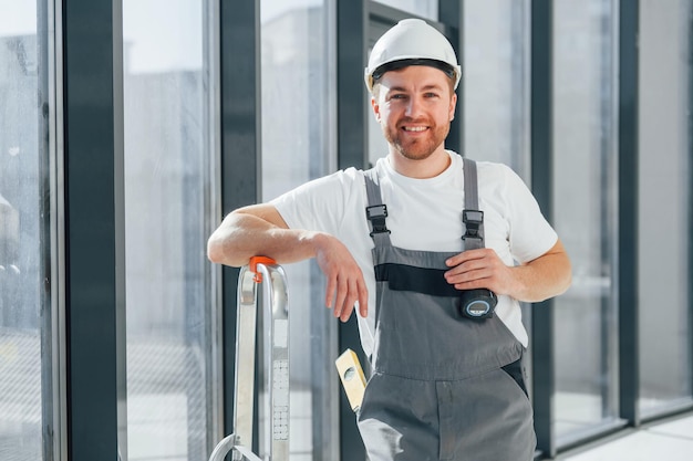 Der lächelnde und posierende Handwerker arbeitet drinnen im modernen Raum