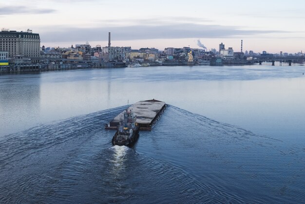 Der Lastkahn schwimmt im Dnepr. Kyiv Stadtlandschaft im Hintergrund.