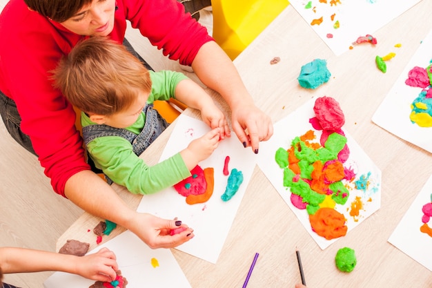 Der Lehrer hilft dem Jungen, eine Figur aus Plastilin auf dem Tisch zu machen