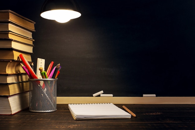 Der Lehrertisch, auf dem das Schreibmaterial liegt, abends unter der Lampe.