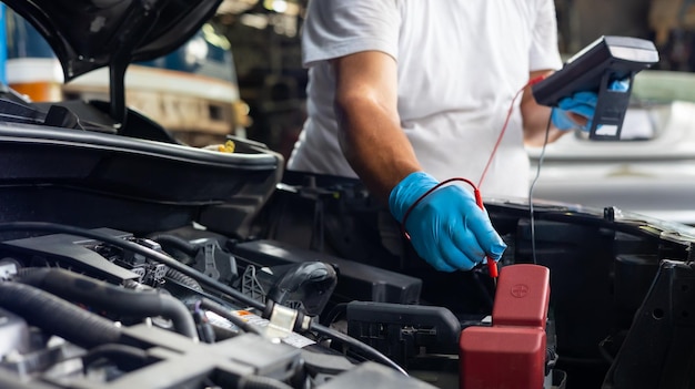 Der leitende Mechaniker verwendet ein Multimeter-Voltmeter, um den Spannungspegel in der Autobatterie in der Autoservice- und Wartungswerkstatt zu überprüfen