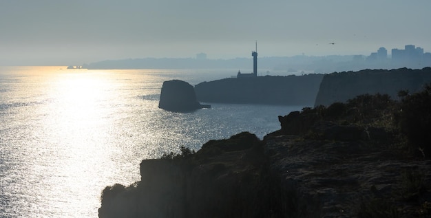 Der Leuchtturm von Ponta do Altar auf einem Vorgebirge. Abendlicher Blick auf die Atlantikküste mit Sonnenreflexion auf der Wasseroberfläche (Ferragudo, Lagoa, Algarve, Portugal).