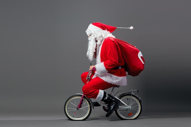 Der lustige Weihnachtsmann mit Sonnenbrille und Weihnachtsgeschenken auf dem Rücken fährt Fahrrad