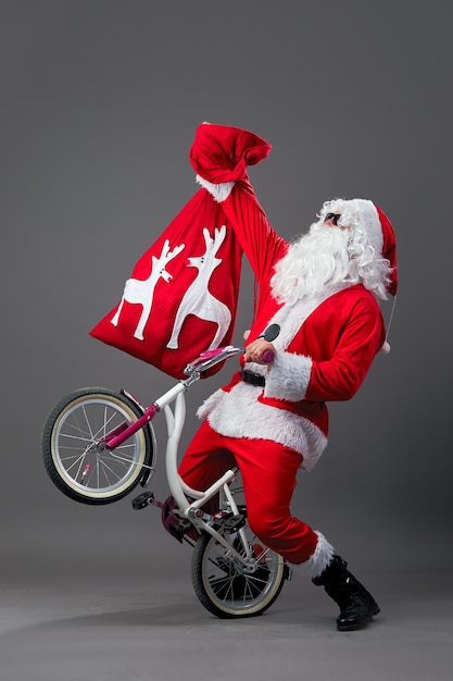 Der lustige Weihnachtsmann mit Sonnenbrille und Weihnachtsgeschenken auf dem Rücken fährt Fahrrad