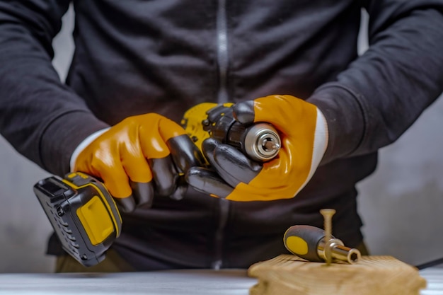 Der männliche Arbeiter hält einen elektrischen Akkuschrauber in der Hand vor dem Hintergrund eines Bauwerkzeugs und einer Betonwand