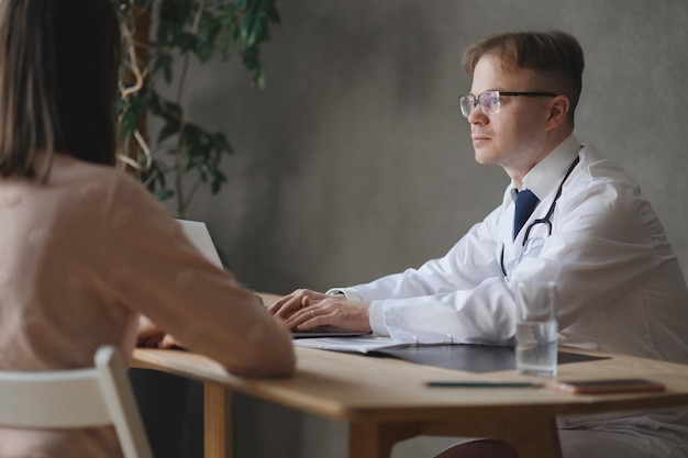 Der männliche Arzt im weißen Kittel im Büro der Klinik spricht mit der medizinischen Diagnosebehandlung von Krankheiten