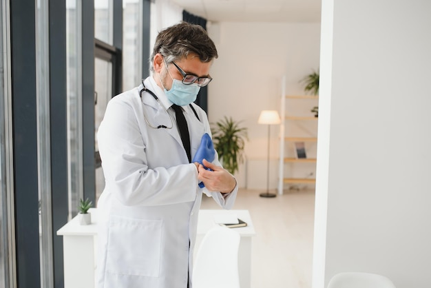 Der männliche Arzt in einer Schutzmaske zieht in der Klinik Handschuhe an