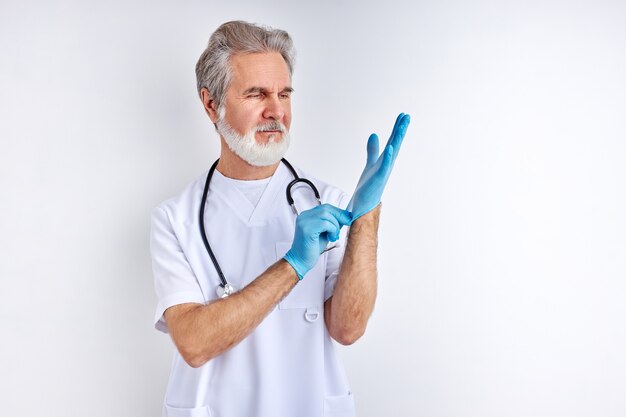 Der männliche Arzt trägt Handschuhe, die sich auf die Arbeit vorbereiten. Er trägt ein weißes Gewand, das im Studio mit Weiß isoliert ist