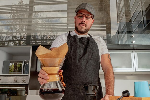 Der männliche Barista macht schwarzen Kaffee in der Chemex-Kaffeemaschine und steht vor der Café-Bar