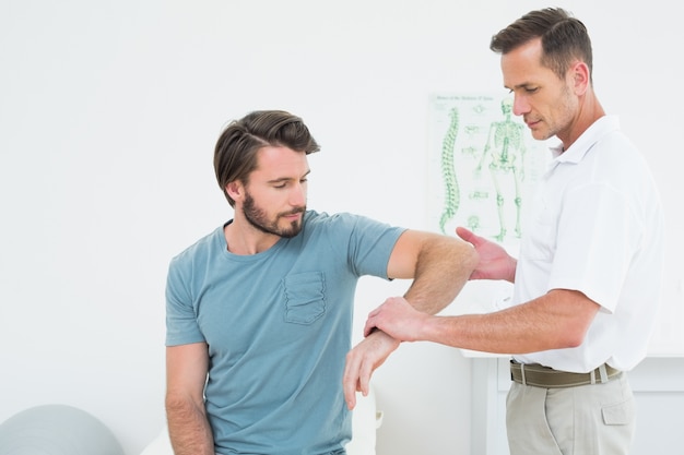 Der männliche Physiotherapeut, der ein Junges überprüft, bemannt Arm