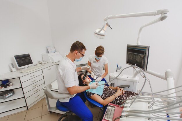 Der männliche Zahnarzt mit einer weiblichen Assistentin hilft bei der Behandlung der Zähne einer Patientin in einer Klinik im Büro