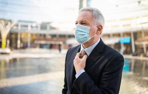 Der Manager passt seine Krawatte an, während er während des Coronavirus und der Covid-Pandemie mit einer Maske im Freien spazieren geht