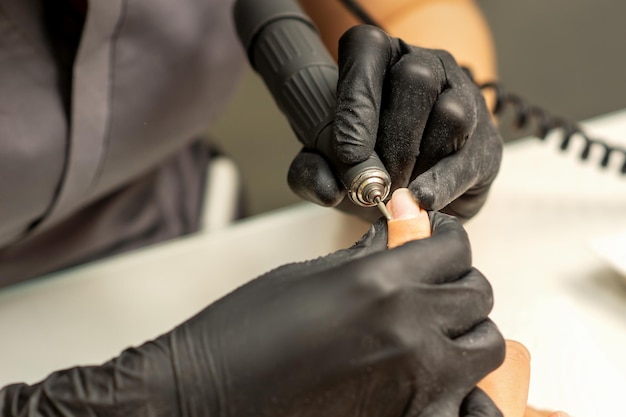 Der Maniküre-Meister verwendet eine elektrische Nagelfeilenmaschine in einem Nagelstudio aus nächster Nähe