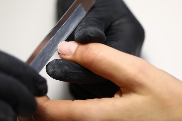 Der Manikürist hält den Finger des Kunden und formt die Nagellänge mit einer Nagelfeile.