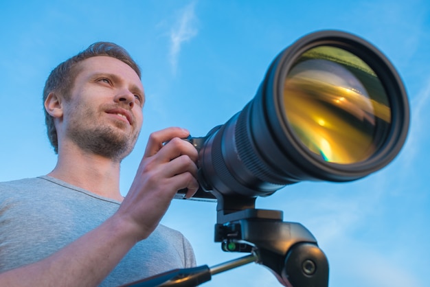 Der Mann arbeitet mit der Kamera auf dem Hintergrund des blauen Himmels