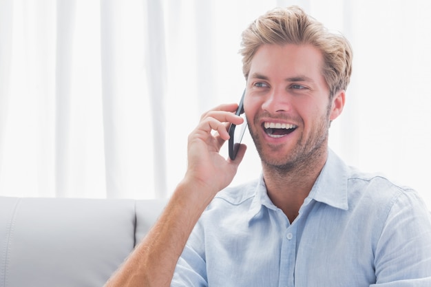 Der Mann, der lacht, während er am Telefon ist, saß auf einer Couch