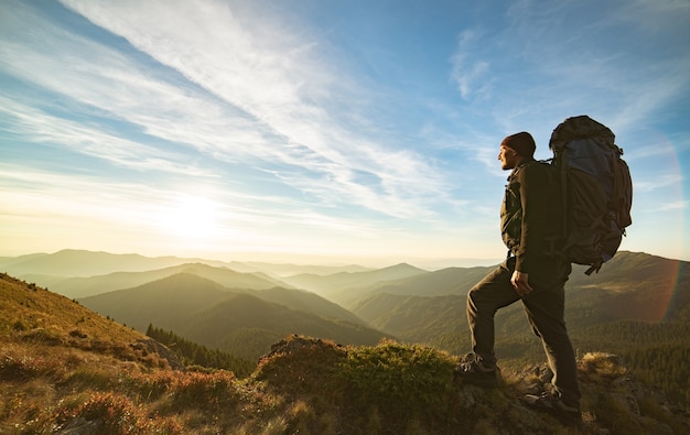 Der Mann, der mit einem Campingrucksack auf dem Felsen mit einem malerischen Sonnenaufgang steht