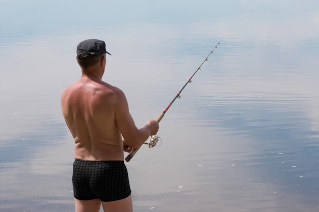 Der Mann fängt Fische beim Spinnen an einem heißen Sommertag auf dem Flussteich