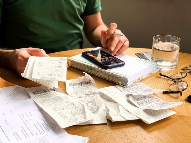 Der Mann führt mit einem Rechner und einem Notizbuch eine Prüfung der Haushaltsausgaben durch. Viele Quittungen und Rechnungen