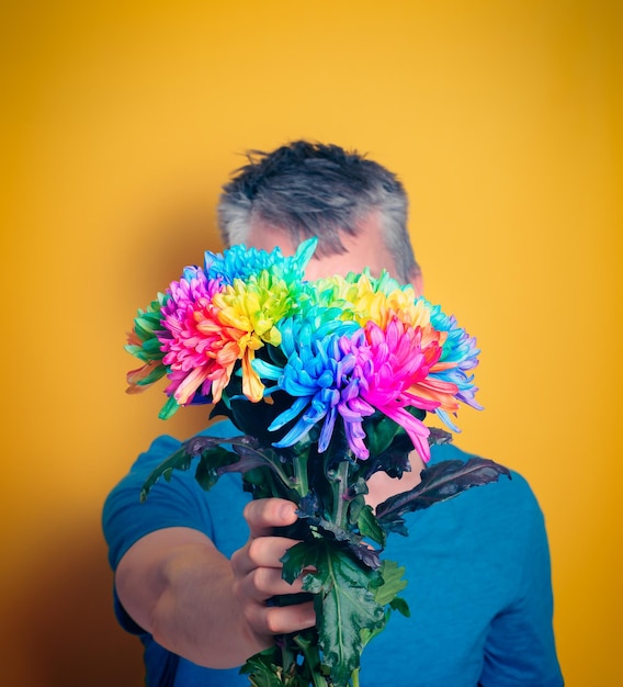 Der Mann hält einen Strauß farbiger Chrysanthemen in die Höhe, die sein Gesicht bedecken