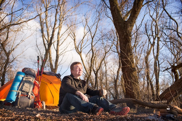 Der Mann im Marsch sitzt neben Zelt und Lagerfeuer