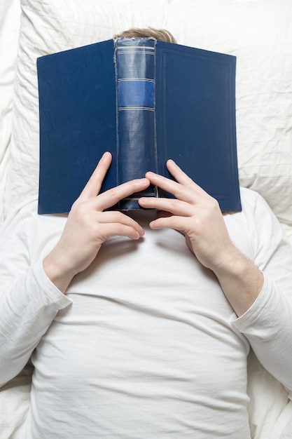 Der Mann im Pyjama schlief beim Lesen mit einem großen Buch im Gesicht ein. Bildungskonzept