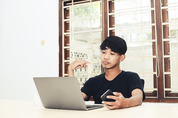 Der Mann im schwarzen asiatischen T-Shirt saß mit trauriger Miene vor dem Laptop