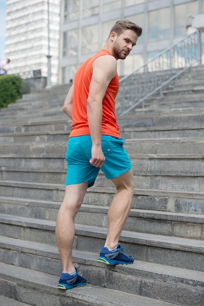 Der Mann in Bewegung auf der Treppe blickt auf den städtischen Hintergrund zurück. Jeder Schritt bringt ihn dem Erfolg näher. Sportlertraining auf der Treppe. Zukünftiges Erfolgskonzept. Bereit, jedes Hindernis zu überwinden. Mann macht Schritt höher.