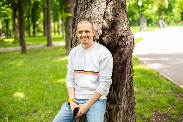 Der Mann lehnte sich an einen Baum und lächelte und schaute am Sommertag im Park in die Kamera