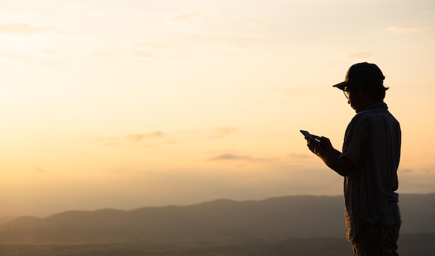 Foto der mann mit dem hut steht mit seinem telefon vor dem sonnenuntergangkopierraum