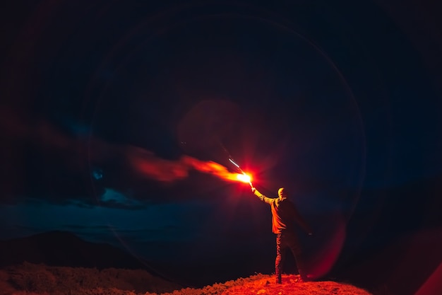 Der Mann mit einem roten Feuerwerksstock, der auf einem Nachtberg steht