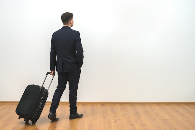 Der Mann mit einer Tasche, der auf dem weißen Wandhintergrund steht