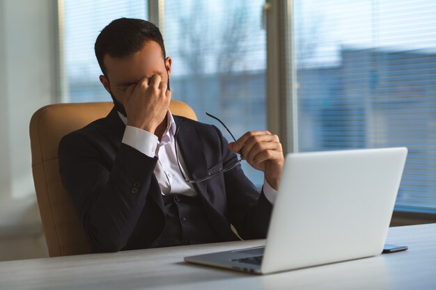 Der Mann mit Kopfschmerzen sitzt mit einem Laptop am Tisch