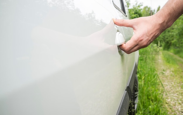 Der Mann öffnet die Tür des Autos mit seiner Hand, die auf der Forststraße steht. Nahansicht.